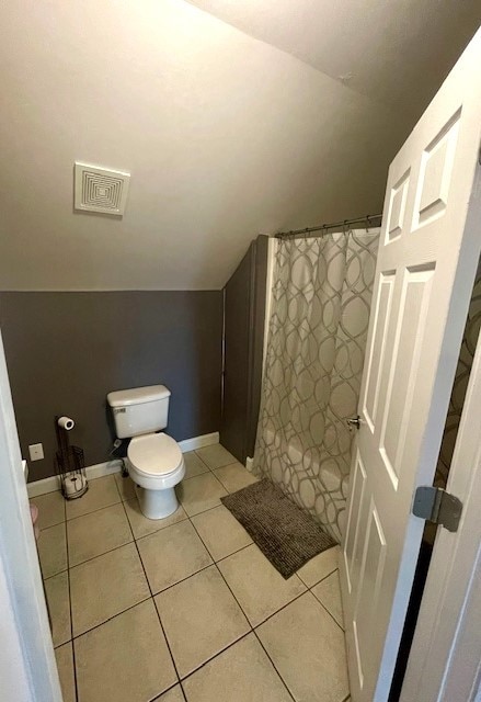 bathroom with a shower with shower curtain, vaulted ceiling, tile patterned floors, and toilet