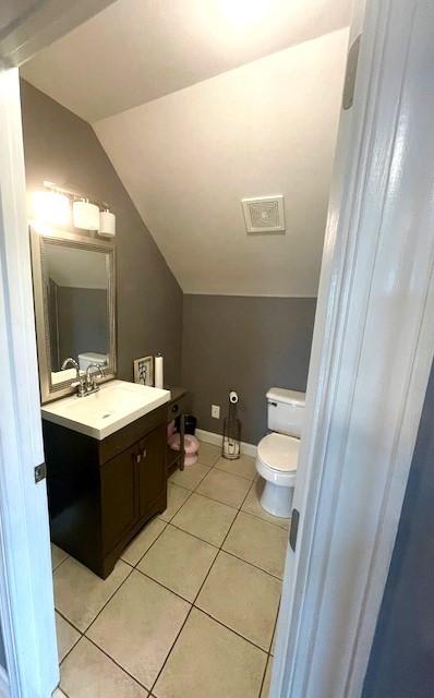 half bathroom featuring vanity, toilet, tile patterned flooring, and lofted ceiling