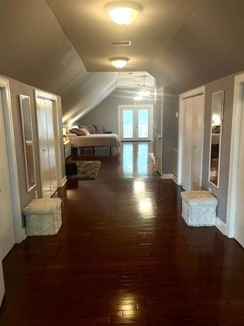 unfurnished bedroom with visible vents, baseboards, two closets, wood finished floors, and lofted ceiling