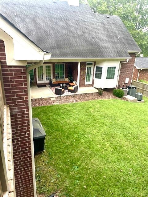 back of property with a yard, brick siding, a patio, and roof with shingles