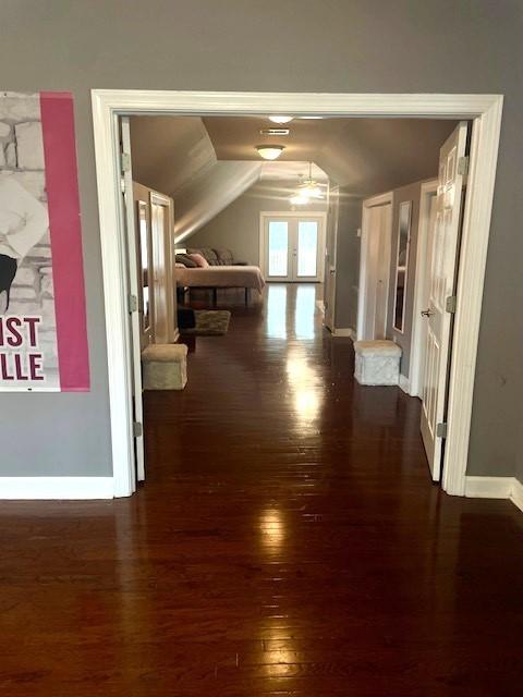 corridor with dark wood-type flooring, french doors, baseboards, and vaulted ceiling