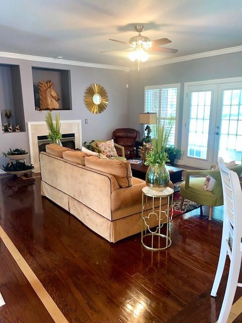 living room featuring ceiling fan, a fireplace, crown molding, wood finished floors, and french doors