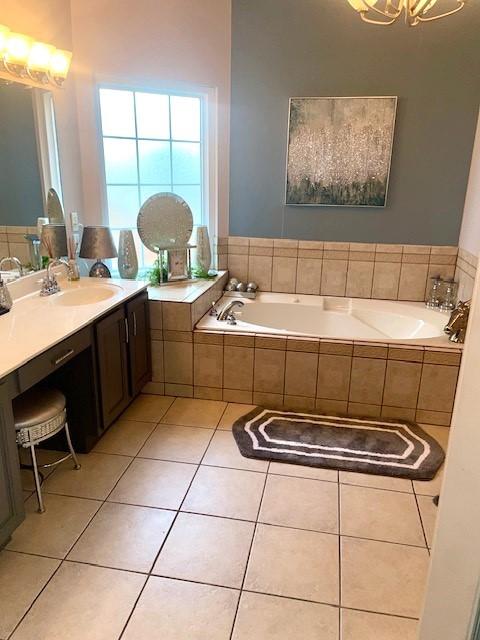 bathroom with tile patterned flooring, vanity, a bath, and a notable chandelier