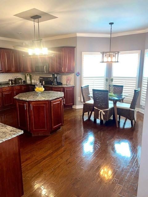 kitchen featuring dark wood-style flooring, backsplash, stainless steel microwave, and decorative light fixtures