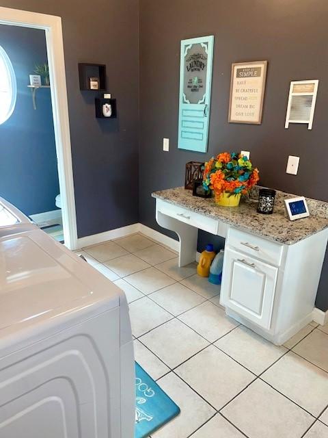 washroom featuring laundry area, separate washer and dryer, light tile patterned flooring, and baseboards