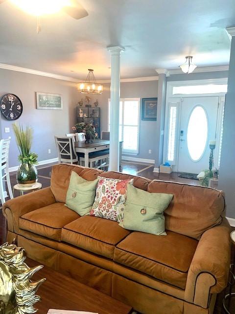 living room with decorative columns, baseboards, ornamental molding, and a notable chandelier