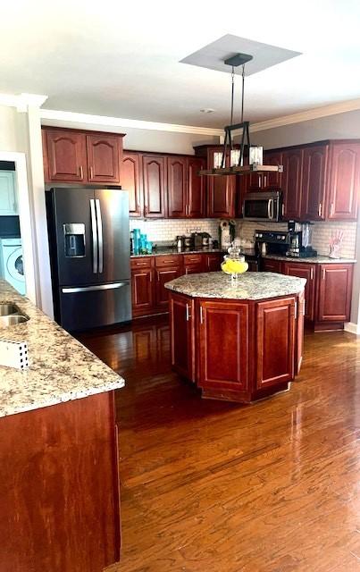 kitchen featuring black electric range oven, stainless steel microwave, reddish brown cabinets, refrigerator with ice dispenser, and washer / dryer