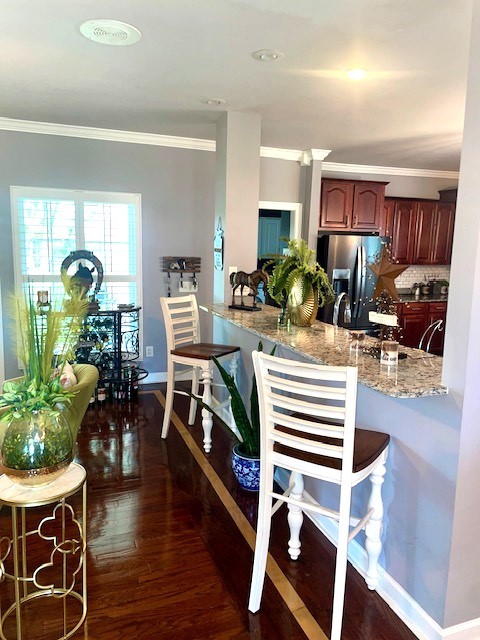 kitchen with stainless steel fridge, light stone counters, dark hardwood / wood-style floors, and crown molding