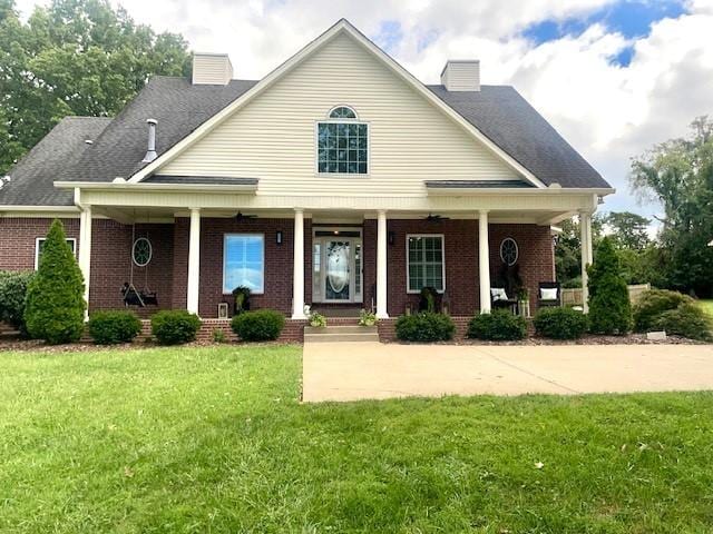 view of front of home with brick siding, a porch, a chimney, and a front lawn