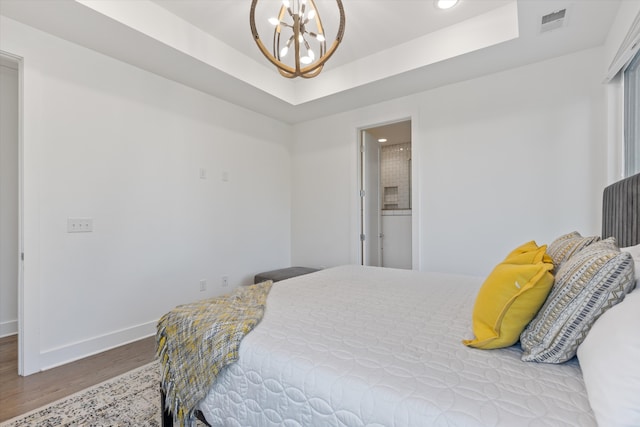 bedroom featuring light wood-type flooring, a raised ceiling, connected bathroom, and an inviting chandelier