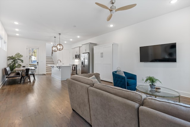 living room featuring ceiling fan with notable chandelier, hardwood / wood-style floors, and sink