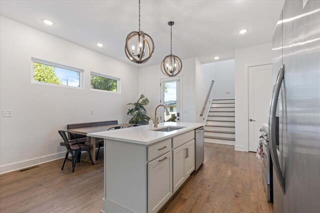 kitchen with stainless steel appliances, a chandelier, sink, wood-type flooring, and an island with sink