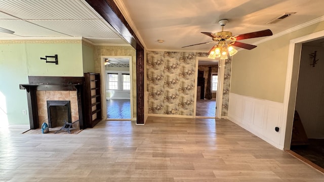 unfurnished living room featuring ceiling fan, light hardwood / wood-style floors, ornamental molding, and a tiled fireplace