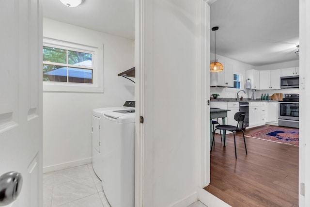 clothes washing area with baseboards, light tile patterned floors, laundry area, independent washer and dryer, and a sink