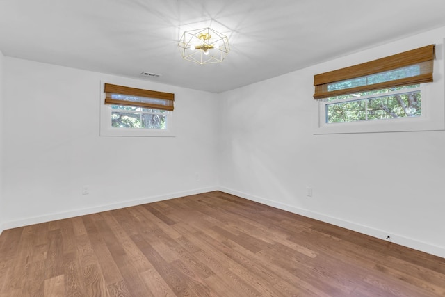 unfurnished room with visible vents, plenty of natural light, wood finished floors, and baseboards