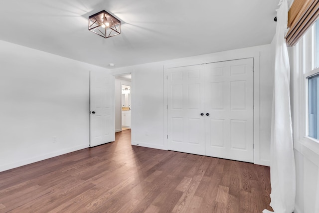 unfurnished bedroom with baseboards, multiple windows, a closet, and wood finished floors