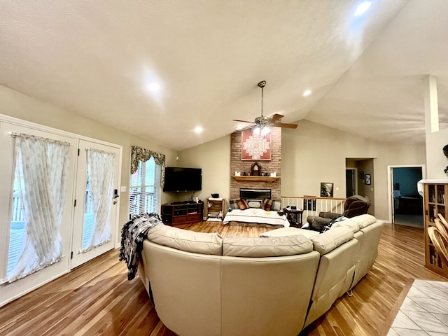 living room with hardwood / wood-style flooring, lofted ceiling, a brick fireplace, and ceiling fan