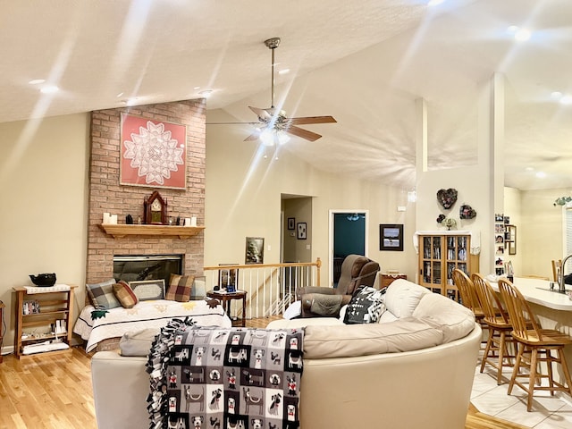 living room featuring a textured ceiling, a fireplace, light hardwood / wood-style flooring, lofted ceiling, and ceiling fan