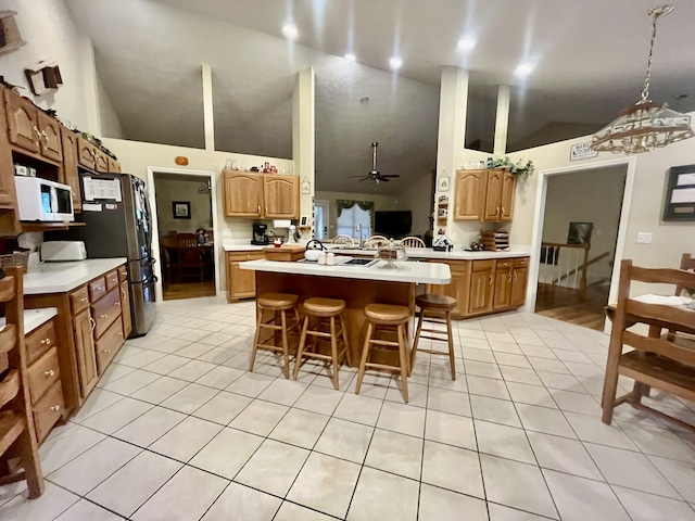 kitchen with light tile patterned floors, stainless steel refrigerator, kitchen peninsula, ceiling fan, and a breakfast bar