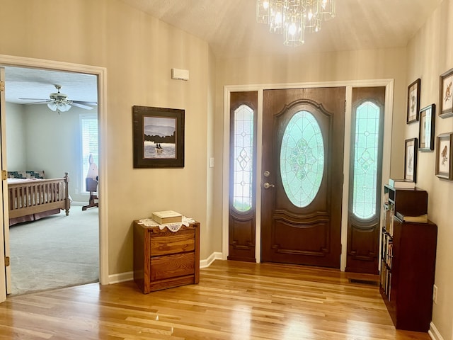 foyer entrance with light wood-type flooring and ceiling fan with notable chandelier