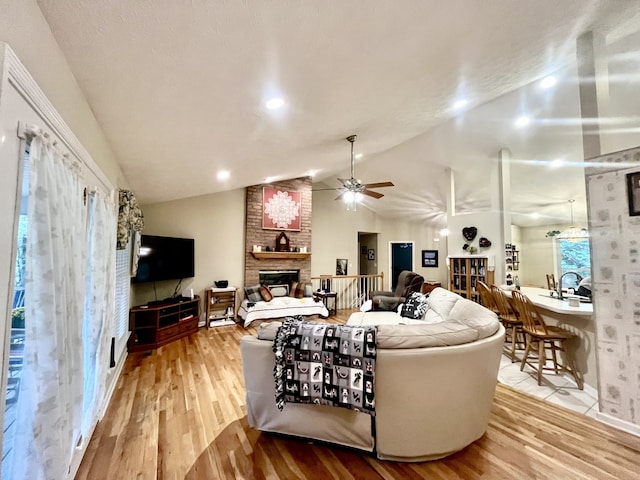 living room with light wood-type flooring, lofted ceiling, a brick fireplace, and ceiling fan