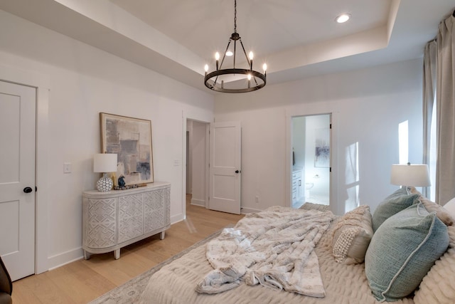 bedroom featuring a chandelier, light hardwood / wood-style flooring, and a raised ceiling