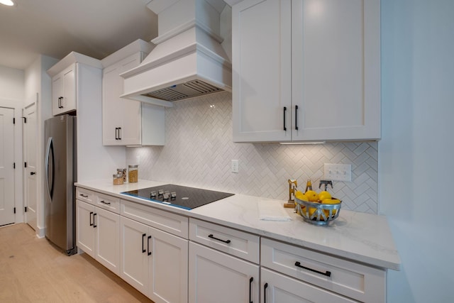 kitchen featuring black electric stovetop, white cabinets, stainless steel fridge, light wood-type flooring, and custom range hood