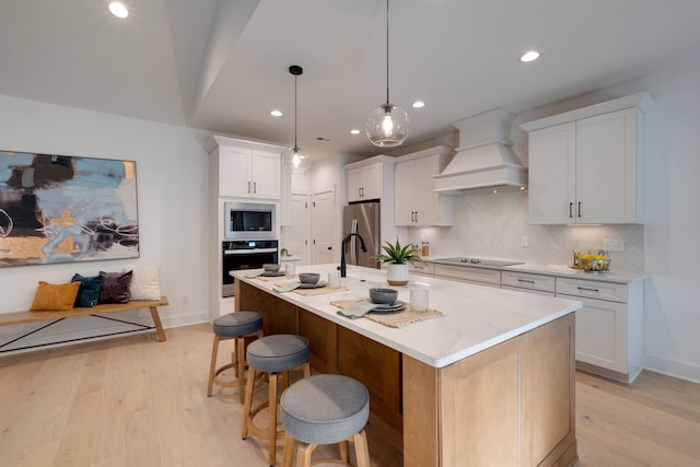 kitchen featuring a center island with sink, white cabinets, hanging light fixtures, custom range hood, and stainless steel appliances