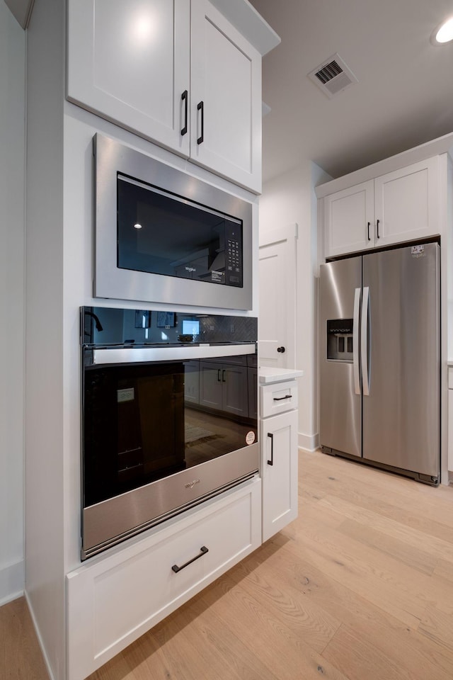 kitchen with light hardwood / wood-style flooring, white cabinets, and appliances with stainless steel finishes