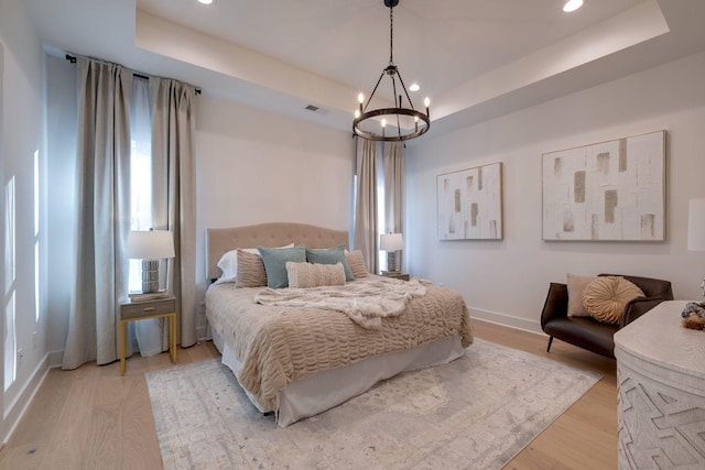 bedroom with a notable chandelier, a tray ceiling, and light hardwood / wood-style flooring