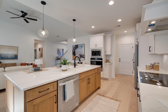 kitchen with light stone counters, light hardwood / wood-style flooring, a center island with sink, white cabinets, and appliances with stainless steel finishes