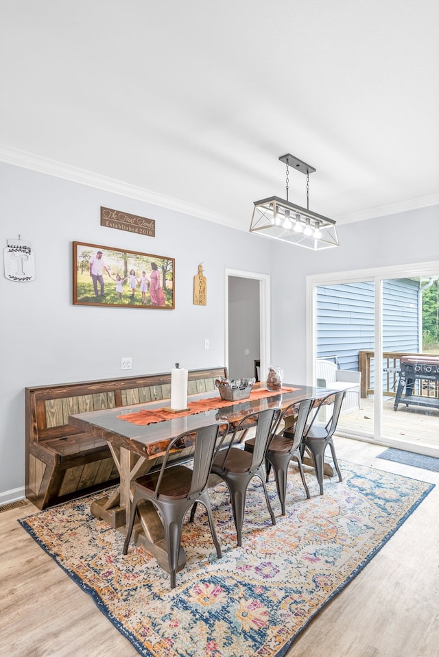 dining space with ornamental molding and light hardwood / wood-style flooring