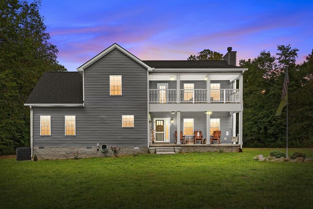 back house at dusk with a yard, central AC, a patio area, and a balcony