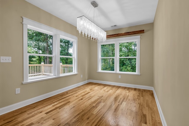 unfurnished room featuring light hardwood / wood-style flooring, a chandelier, and a healthy amount of sunlight