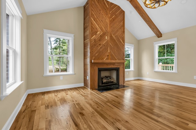 unfurnished living room featuring light hardwood / wood-style flooring, a large fireplace, beamed ceiling, and a healthy amount of sunlight