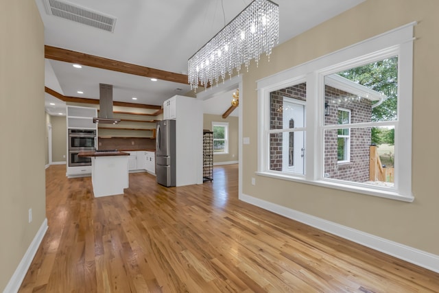 unfurnished living room with a notable chandelier, beam ceiling, and light hardwood / wood-style floors