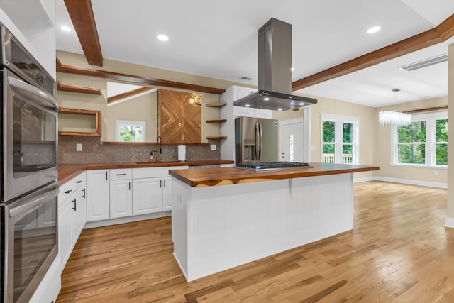 kitchen with wood counters, stainless steel appliances, island exhaust hood, and a healthy amount of sunlight