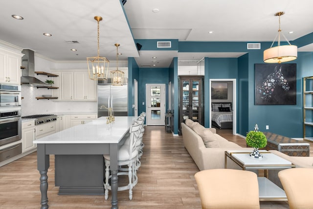 kitchen with light hardwood / wood-style flooring, appliances with stainless steel finishes, wall chimney exhaust hood, an island with sink, and a breakfast bar area