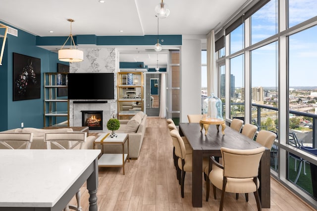 dining area with light wood-type flooring, expansive windows, and a high end fireplace