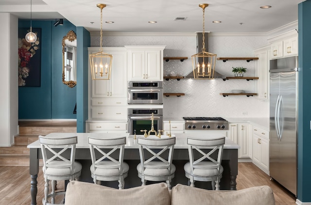 kitchen featuring a kitchen island with sink, decorative light fixtures, stainless steel appliances, and light hardwood / wood-style floors