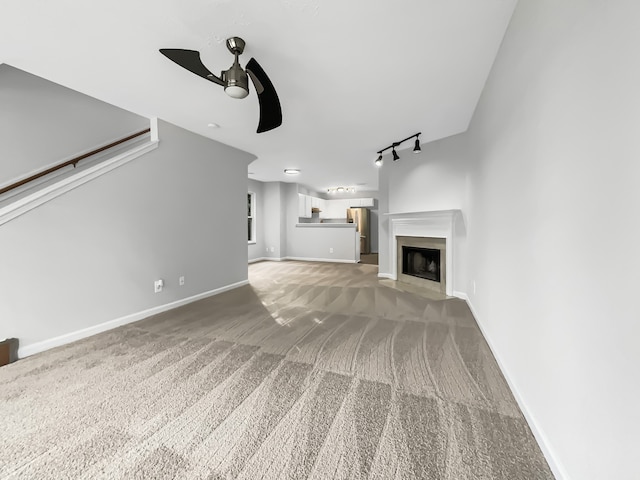 unfurnished living room with rail lighting, ceiling fan, and carpet