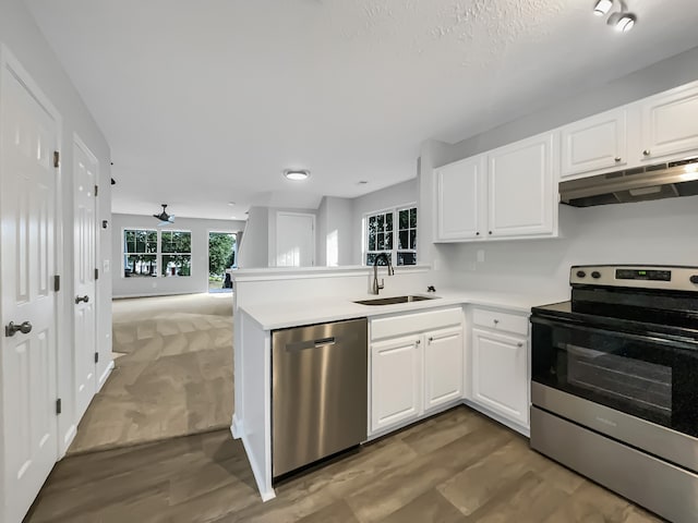 kitchen featuring hardwood / wood-style floors, white cabinetry, kitchen peninsula, sink, and appliances with stainless steel finishes