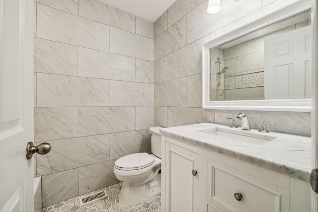 bathroom with vanity, toilet, tile walls, and a tile shower