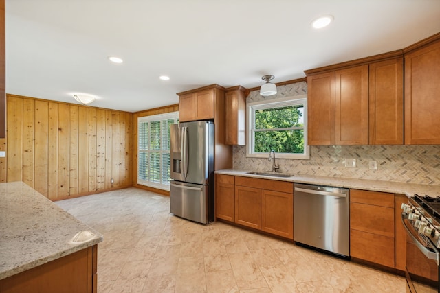 kitchen with crown molding, light stone countertops, stainless steel appliances, sink, and wood walls