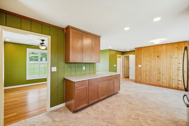 kitchen featuring light hardwood / wood-style flooring, ceiling fan, light stone countertops, and wooden walls