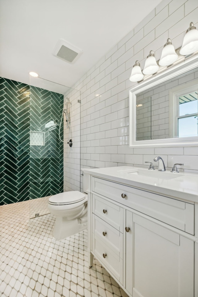 bathroom with vanity, toilet, a tile shower, and tile walls