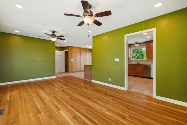 empty room with ceiling fan, wooden walls, sink, and light hardwood / wood-style flooring