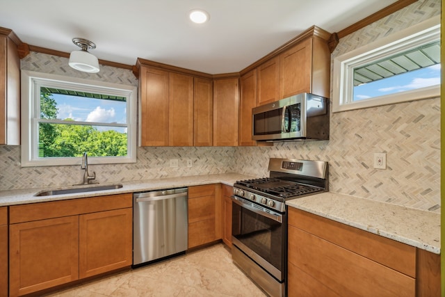 kitchen with appliances with stainless steel finishes, light stone counters, sink, tasteful backsplash, and ornamental molding