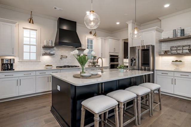 kitchen featuring a kitchen island with sink, white cabinetry, stainless steel appliances, dark hardwood / wood-style floors, and custom range hood