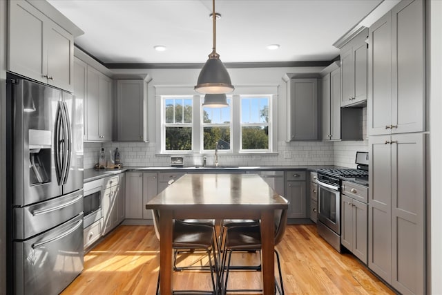 kitchen featuring gray cabinets, light hardwood / wood-style floors, decorative backsplash, appliances with stainless steel finishes, and decorative light fixtures